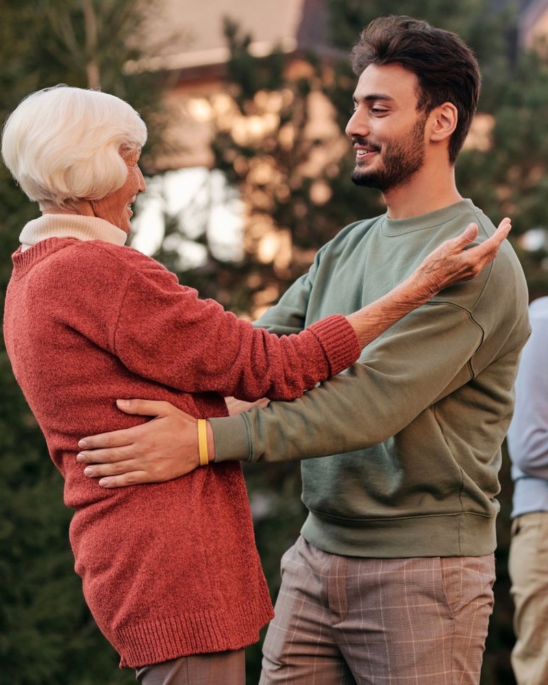 An older woman in a red sweater greeting her son with a hug in a garden